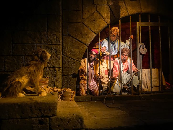 Pirate animatronics reaching through jail bars with a bone to try and entice an animatronic dog with a key in it's mouth to them. This scene comes from the end of the Pirates at the Caribbean ride.
