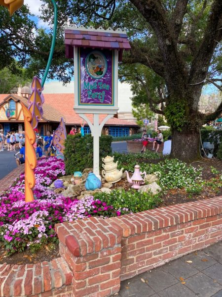 The Sign outside the Mad Tea Party, which is surrounded by blooming flowers. 