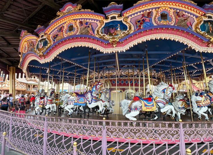 Image of Prince Charming's Carrousel. With plastic horses done up in vibrant costuming with depictions of classic Disney stories at the top.